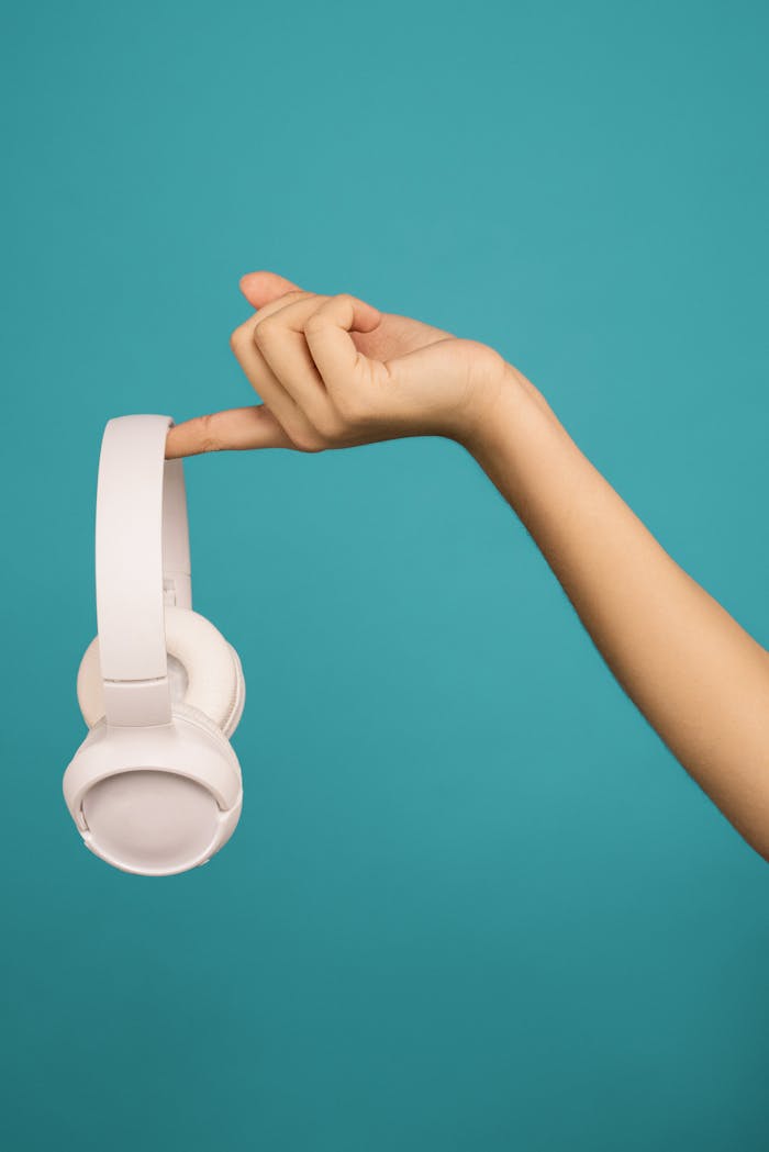 A hand gracefully holds wireless headphones against a teal background.